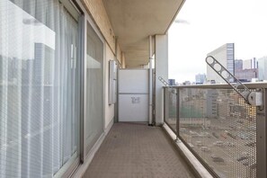 Un corridoio stretto con una ringhiera metallica, una porta con un cartello e una vista sulla città sullo sfondo.