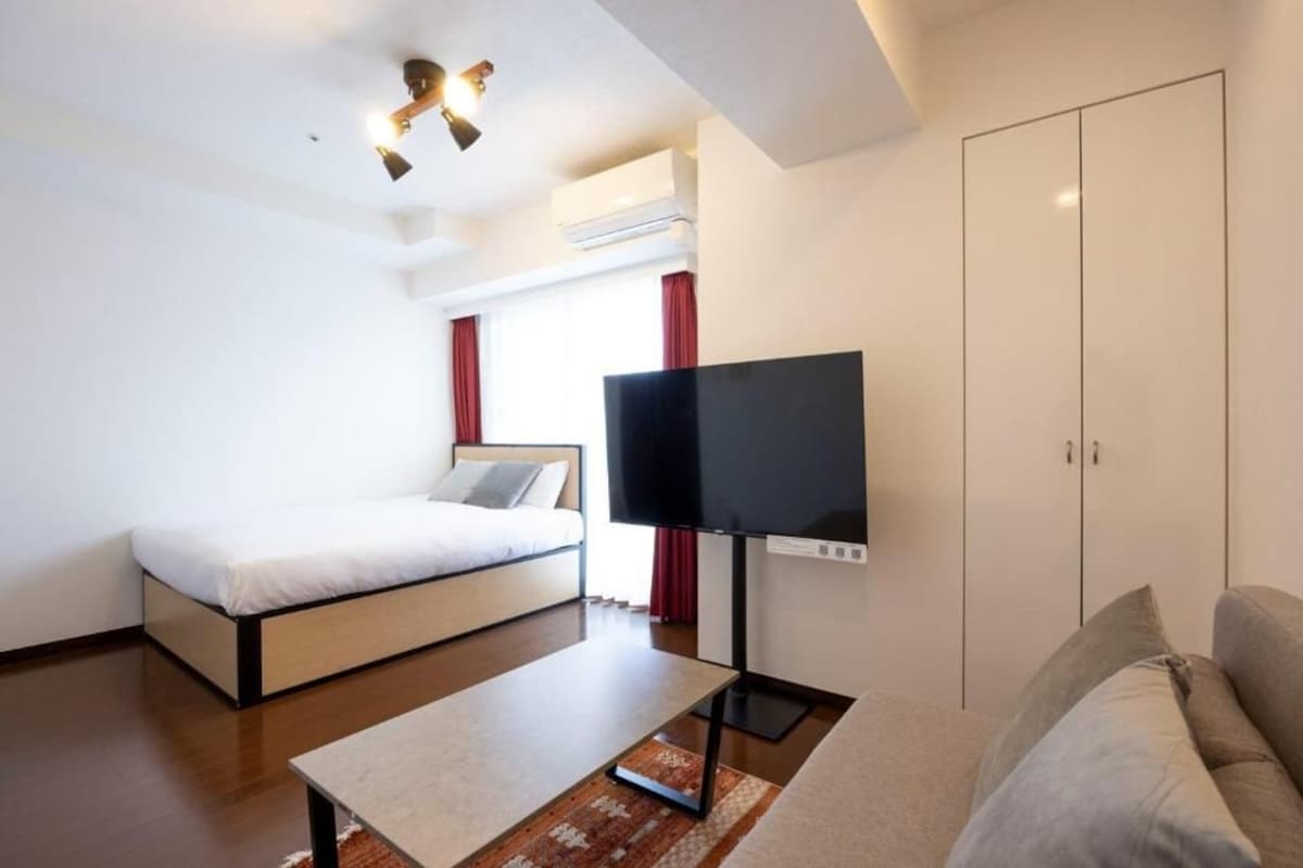 Una camera d'albergo con un letto, una TV a schermo piatto, una poltrona e un armadio.