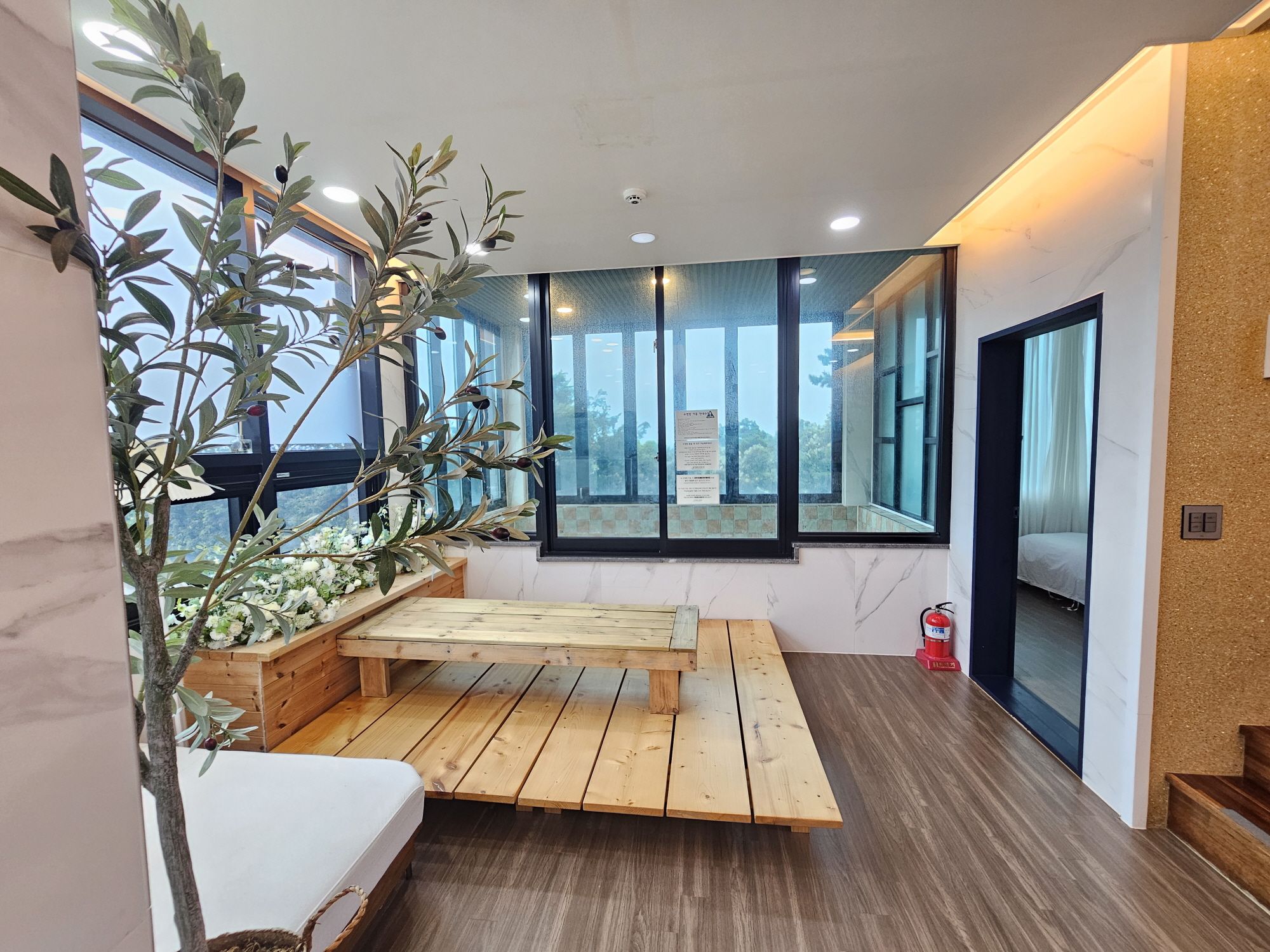 A modern interior with a wooden bench, large windows, and a view of the outdoors.