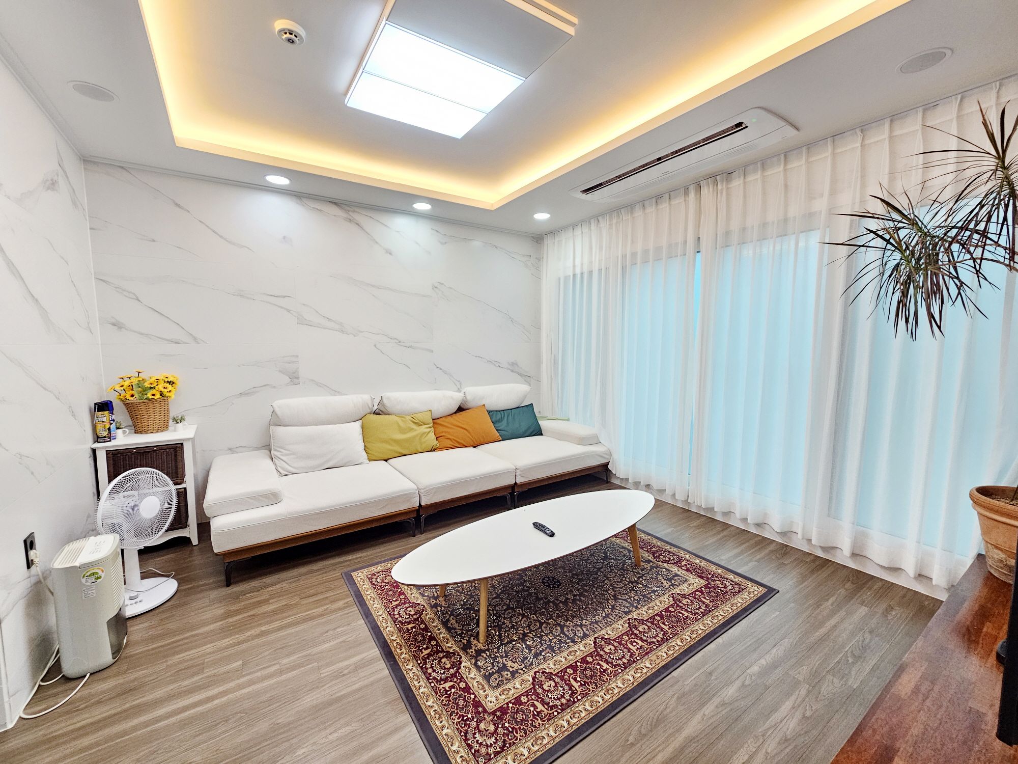 Una sala de estar moderna con un sofá, una mesa de centro, un ventilador y una planta en maceta.