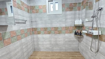 Zona de ducha con pared de azulejos, una ventana y repisas con artículos de aseo.