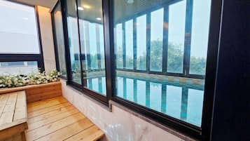 Un banco de madera y un ventanal con vistas a una piscina y árboles.