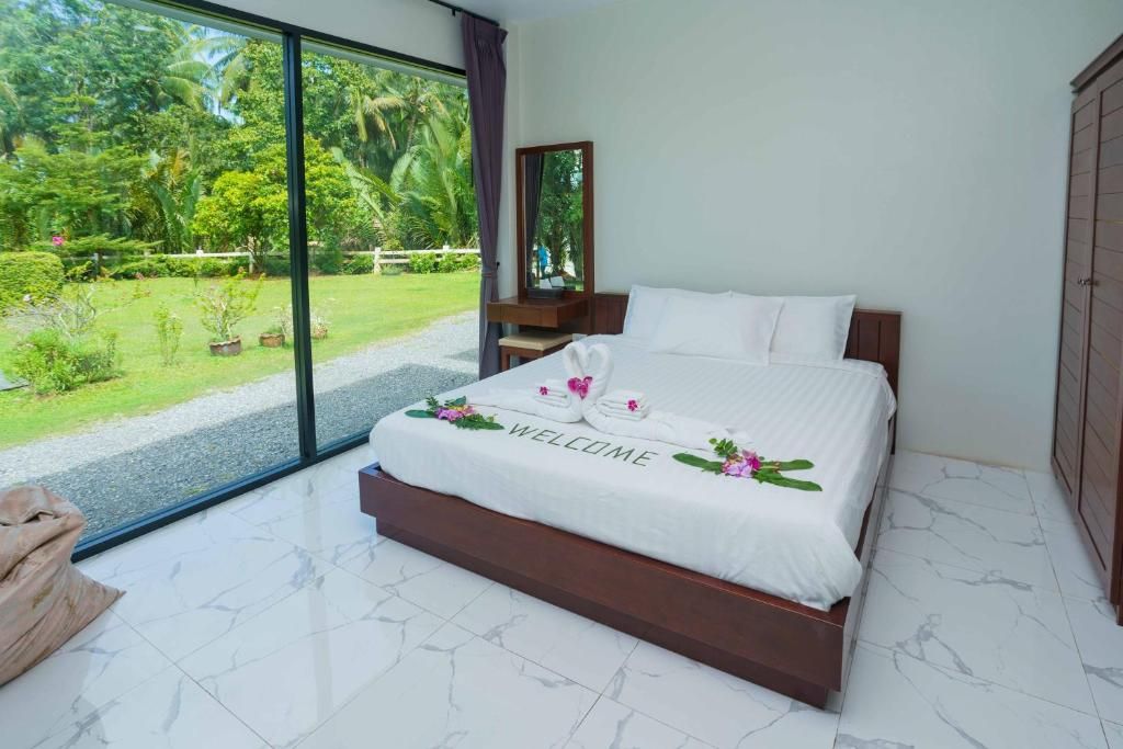 A hotel room with a large bed, a nightstand, a mirror, and a view of a lush garden through a sliding glass door.