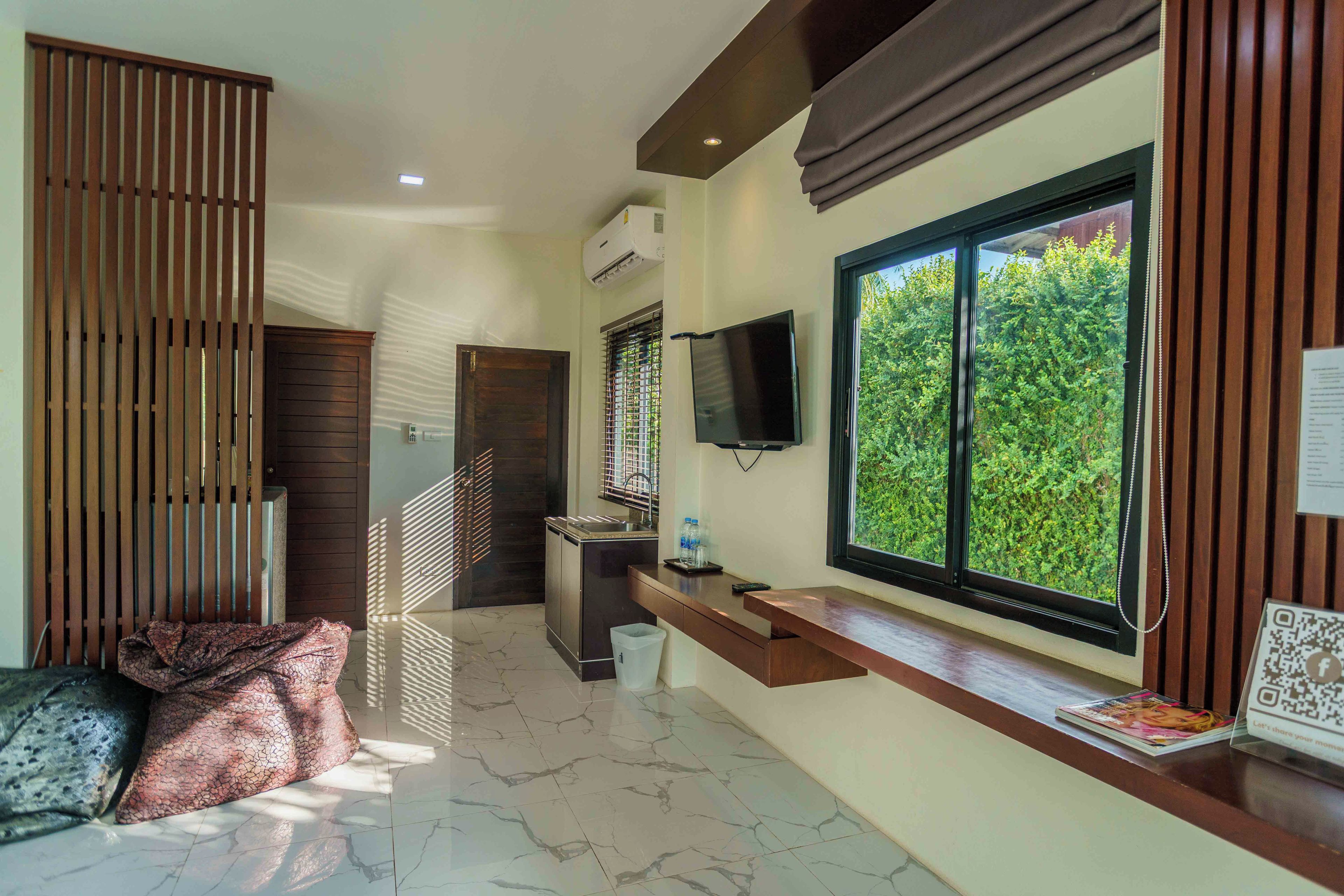 A modern hotel room with a large window, a flat-screen TV, a built-in sink, and a small seating area.