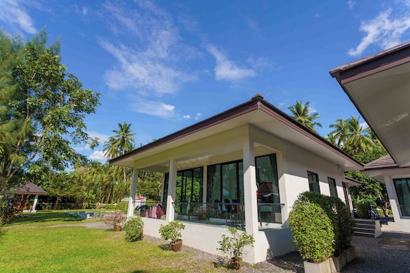 A modern house with a covered porch, large windows, and a well-maintained garden with palm trees and shrubs.