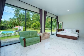 A modern bedroom with a large window, a green sofa, a bed, and a view of a swimming pool.