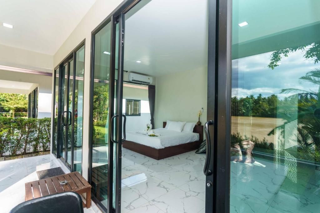 A modern bedroom with a large bed, a small table, and a glass door leading to a balcony.