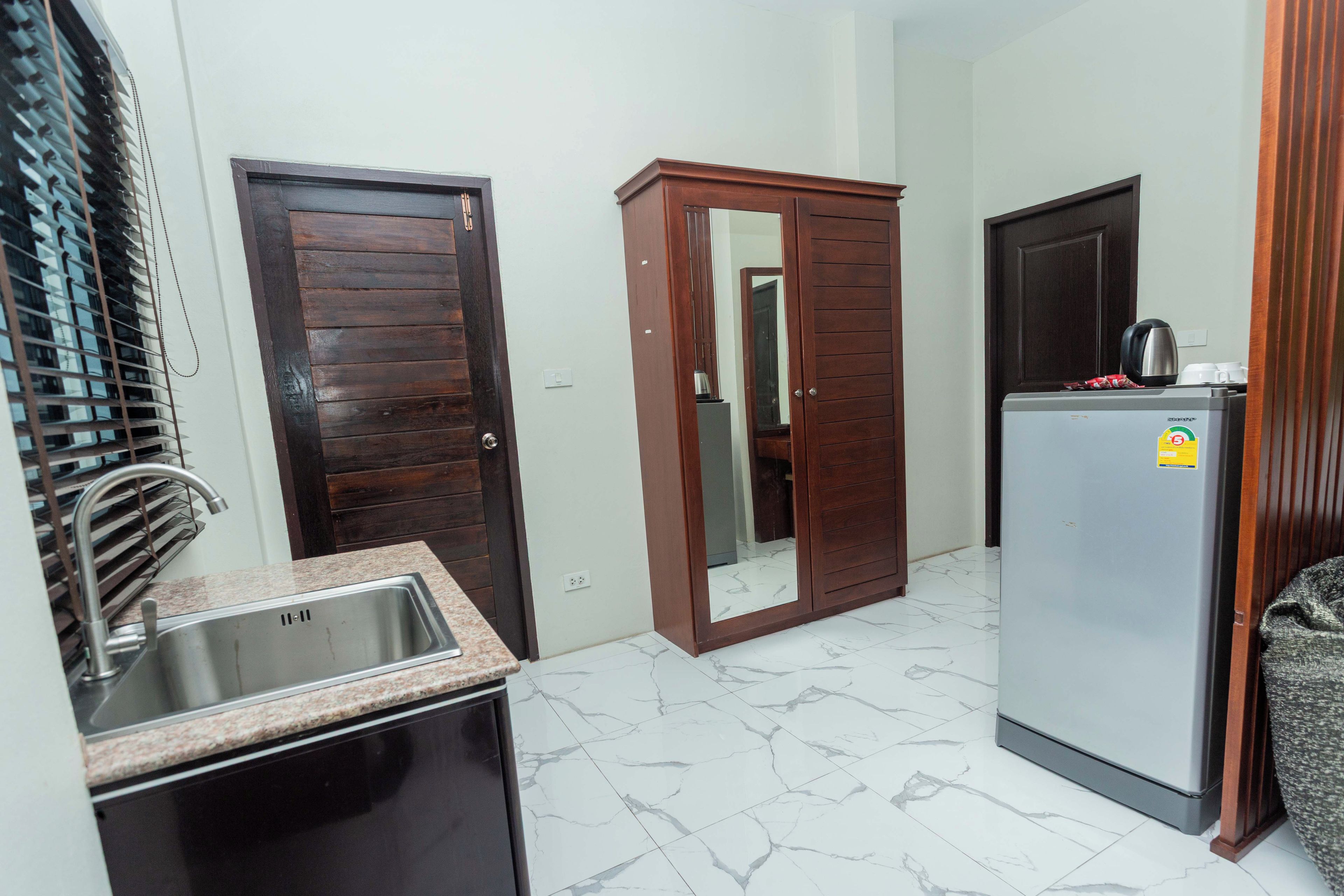 A compact kitchen with a stainless steel sink, a built-in refrigerator, and a wooden wardrobe with a mirror.