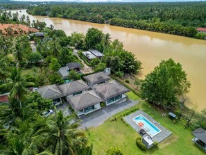 A residential area with a swimming pool, surrounded by lush greenery and a river. - Suanson Villa Koh SaNher (Mueang)