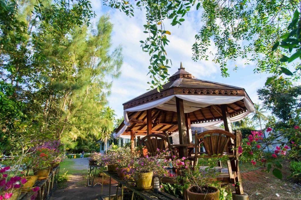 A gazebo with a wooden roof and white drapes, surrounded by potted plants and flowers.