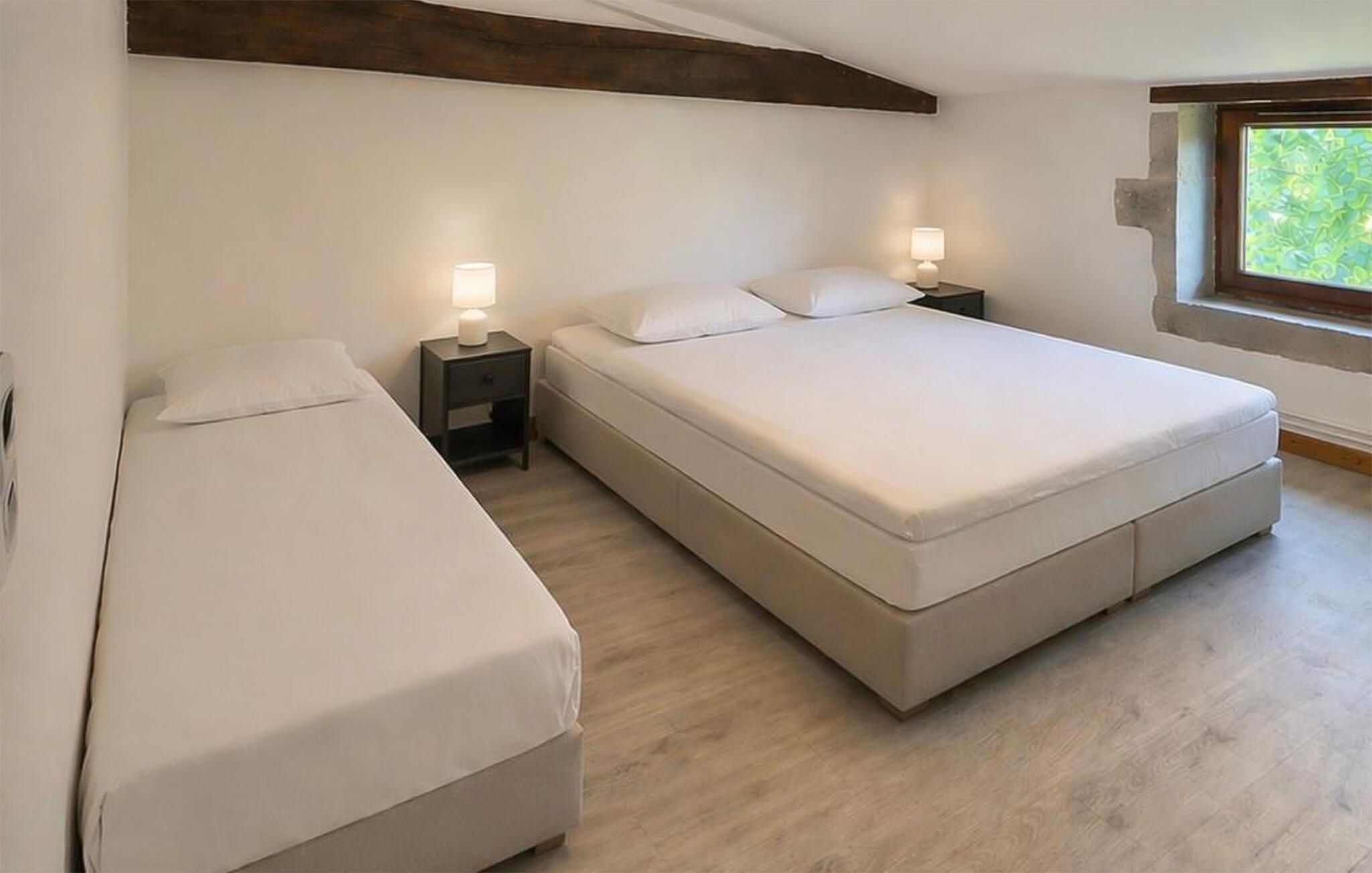 Une chambre à coucher avec un grand lit, deux tables de chevet avec des lampes et une fenêtre donnant sur un paysage verdoyant.