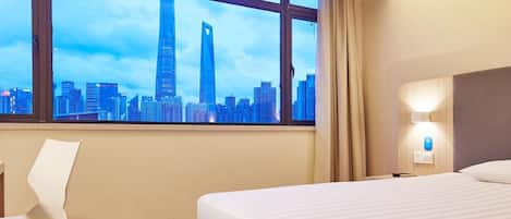 A hotel room with a large window, a bed, a chair, and a wall-mounted light.