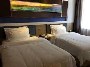 A hotel room with two beds, a nightstand with a phone, and a wall-mounted TV displaying a nature scene. - Lavande Hotel (Lanzhou)