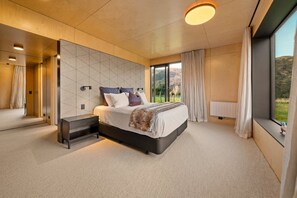 Een moderne slaapkamer met een groot bed, een nachtkastje, een wandtelevisie en uitzicht op het omliggende landschap.