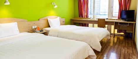 A hotel room with two beds, a desk with a television, and a window with curtains.
