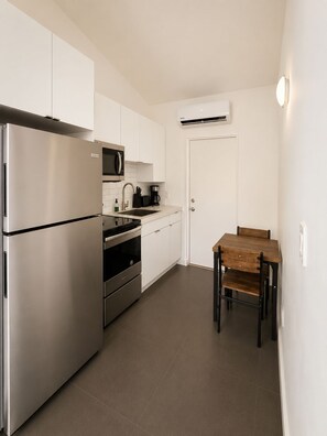 A compact kitchen with stainless steel appliances, a microwave, a coffee maker, and a dining table with chairs. - Private-Patio Studio near Miami Beach (Miami)