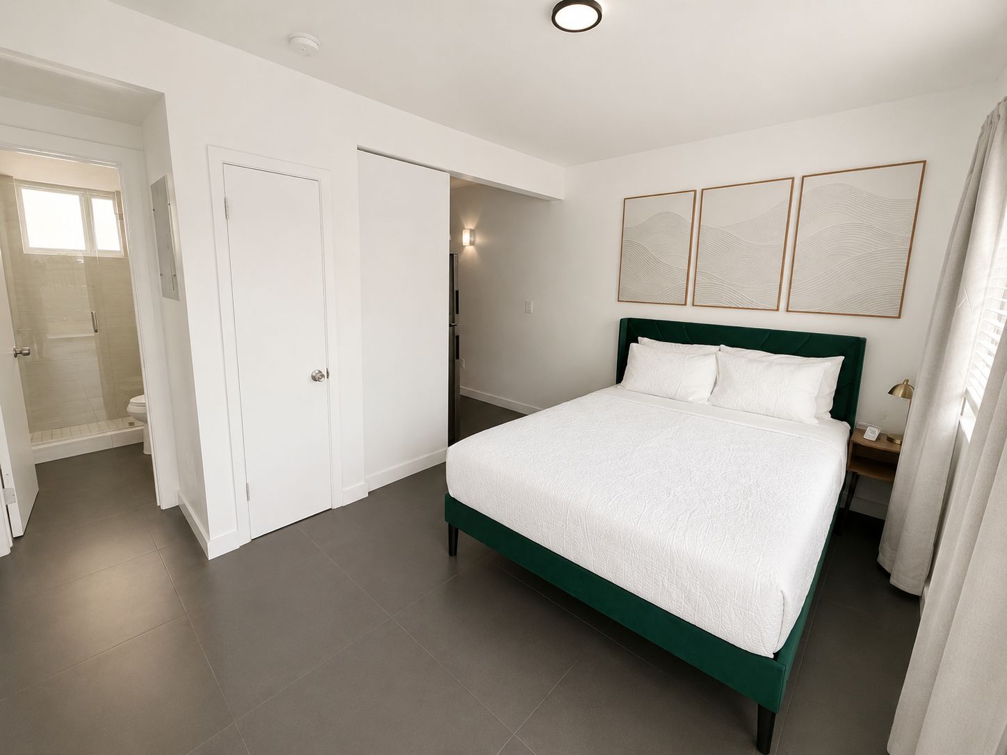 Une chambre d’hôtel comprenant un lit, un dressing, une salle de bain avec douche et un luminaire fixé au mur.