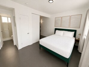 Habitación de hotel con cama, vestidor, baño con ducha y lámpara fijada a la pared.