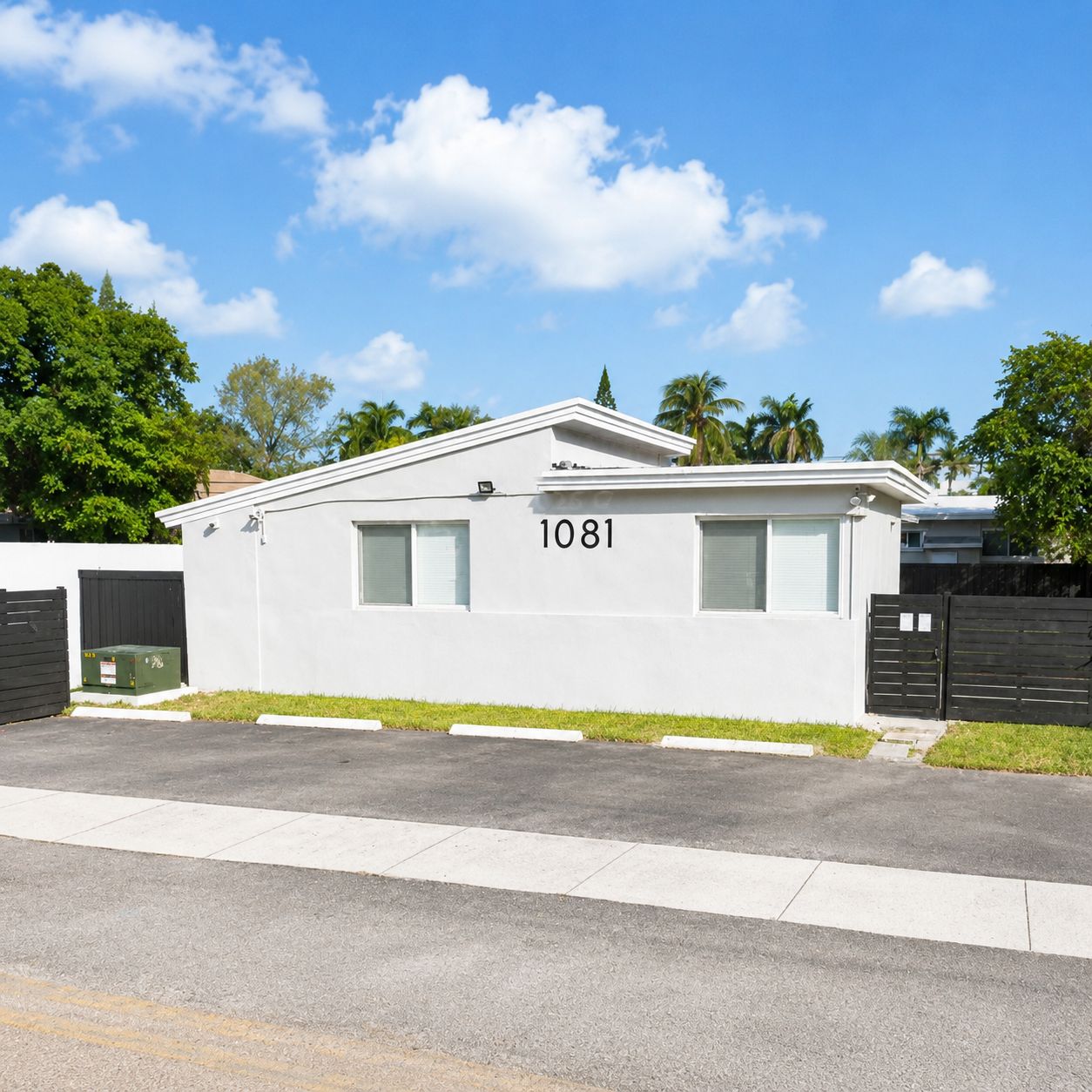A modern single-story building with the number 1081, surrounded by a well-maintained lawn and a gated driveway.