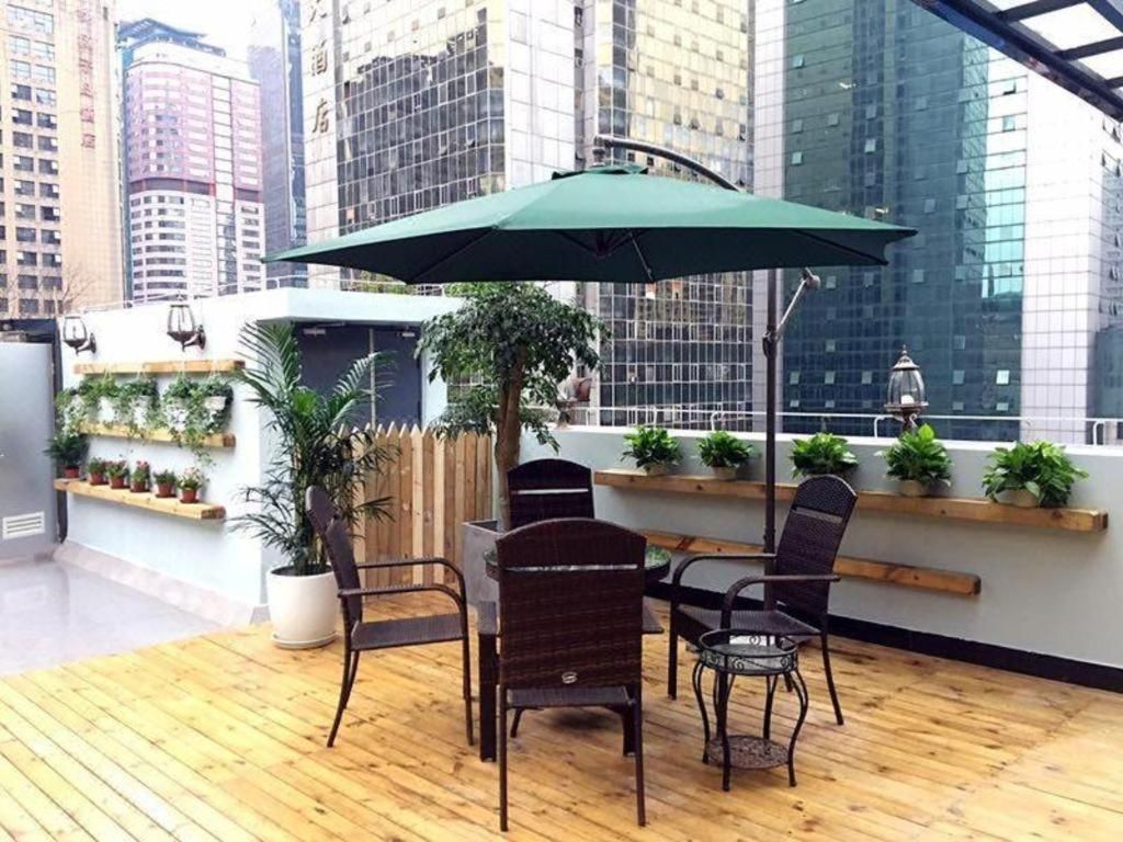 Un área de estar al aire libre con una mesa, sillas, un paraguas verde y plantas en macetas.