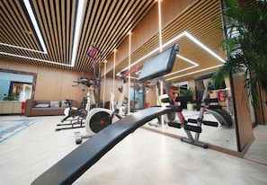 A gym with various exercise equipment, a wooden ceiling, and a large mirror. - Xana Hotelle (Jinan)