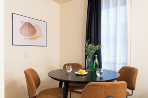 A dining area with a round table, four chairs, a framed artwork, a vase with plants, and a bottle. - Granado Roppongi (Minato-ku)