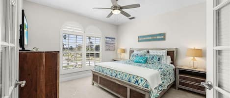 A bedroom with a bed, a ceiling fan, a nightstand, a lamp, and a view through the window.