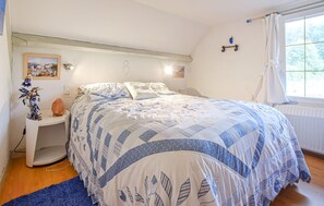 Ett sovrum med en säng, ett nattduksbord, en lampa, en vägghylla och ett fönster med gardiner.