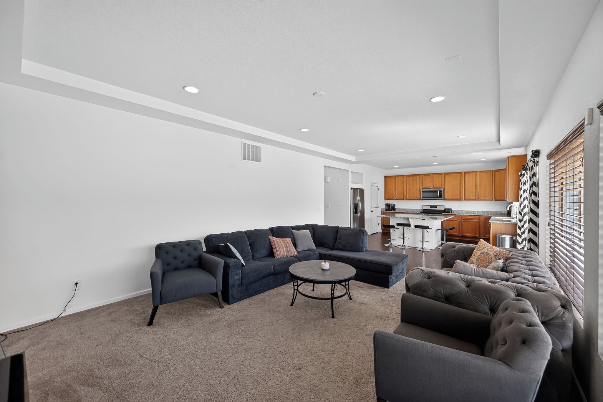 A modern living room with a sectional sofa, a round coffee table, and a kitchen area with wooden cabinets and a bar.