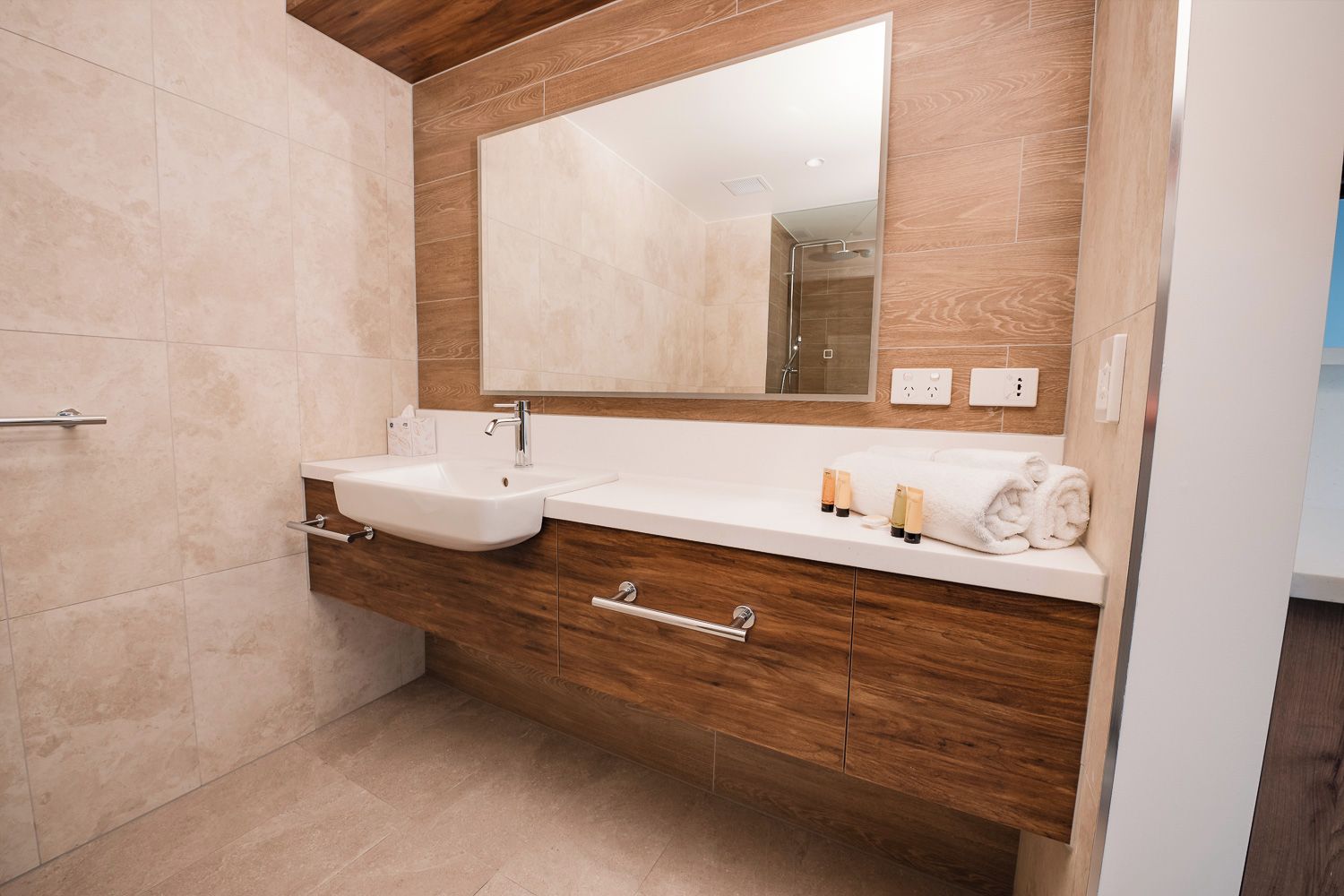 A modern bathroom with a double sink, wooden vanity, and a large mirror.