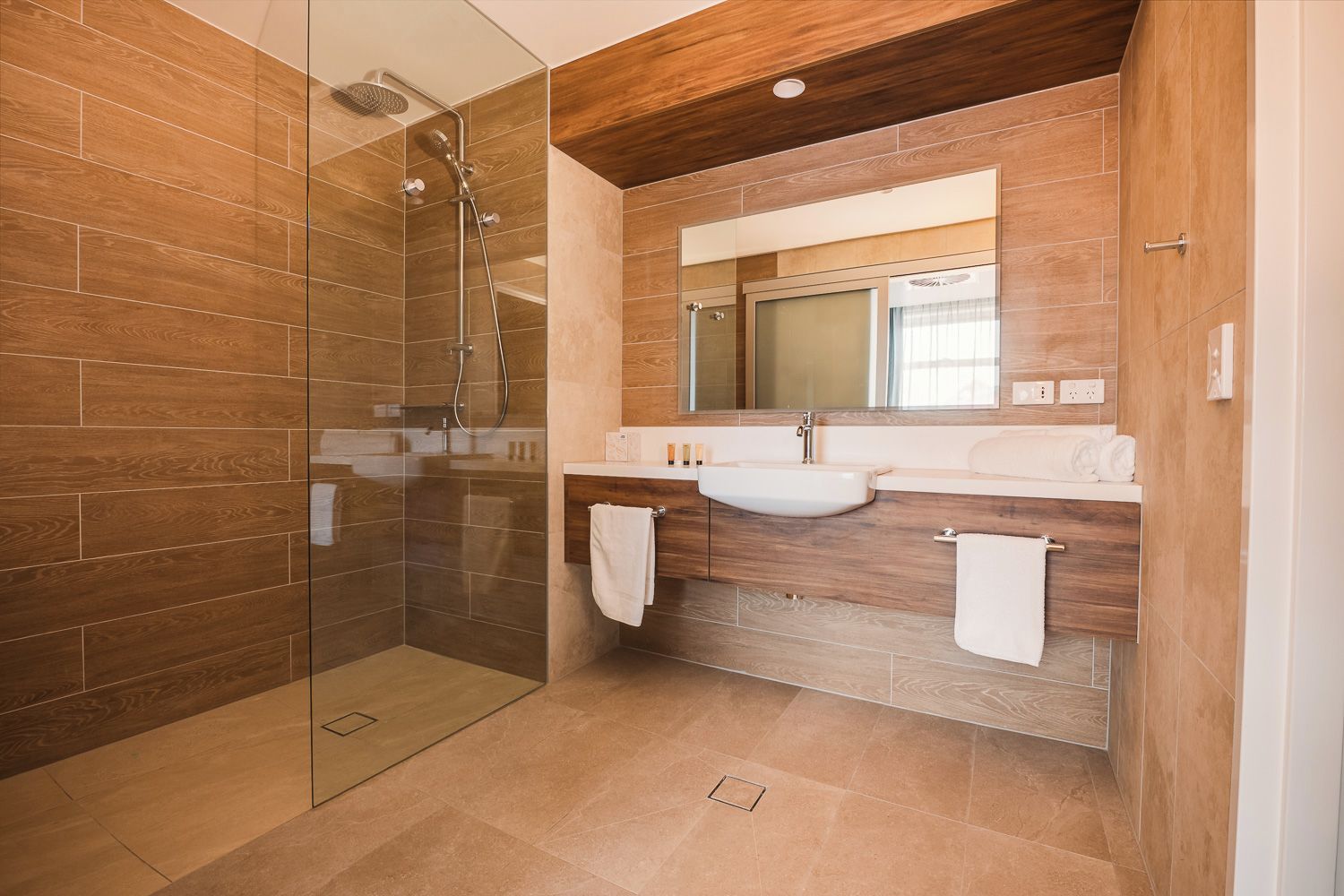 Un bagno moderno con cabina doccia in vetro, pannelli in legno e un mobile lavabo con specchio e lavandino.