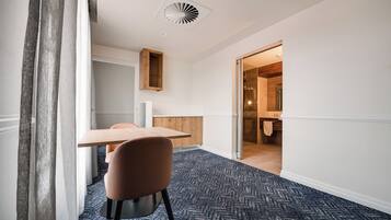 Habitación de hotel con una mesa de madera, una silla, alfombra estampada y vista al baño.