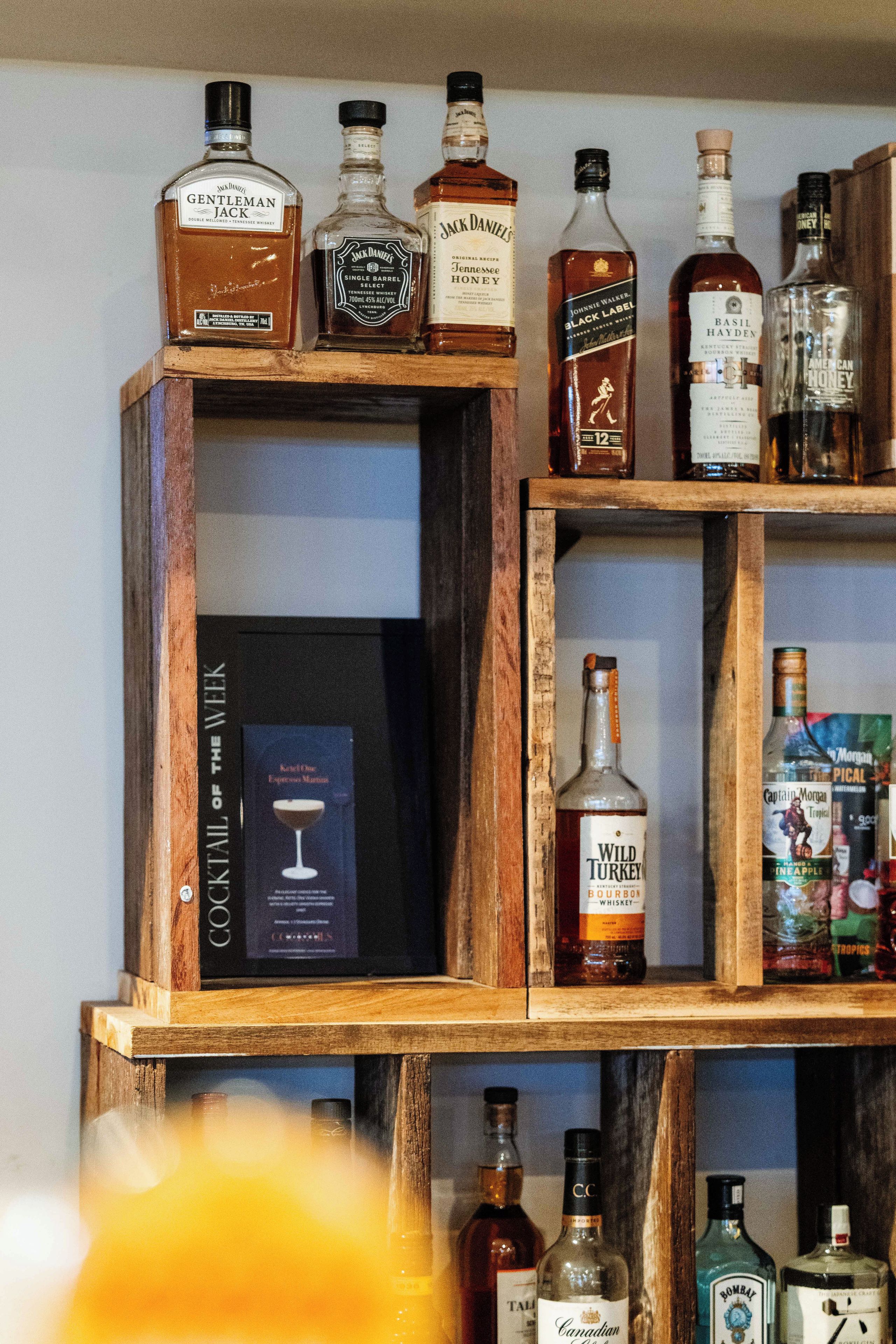 A wooden shelf with various bottles of alcohol, including whiskey and other spirits.