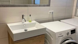 Casa de banho moderna com uma pia branca, espelho, janela e máquina de lavar branca.