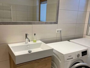 Un baño moderno con un lavabo blanco, un espejo, una ventana y una lavadora blanca.
