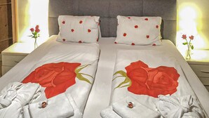 Uma cama de casal com roupa de cama e almofadas estampadas com rosas, cabeceira cinza e mesas de cabeceira com luminárias.