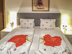 Una cama doble con ropa de cama y almohadas estampadas con motivos de rosas, un cabecero gris y mesitas de noche con lámparas.
