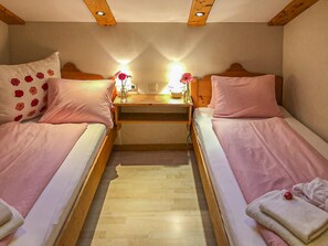 A bedroom with two single beds, a wooden headboard, a nightstand with a lamp, and a small table with flowers.