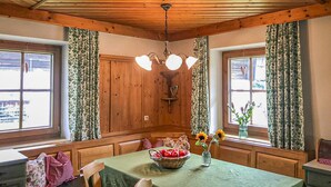 Quarto com vigas de madeira no teto, um candelabro, uma mesa com toalha verde e cortinas florais.