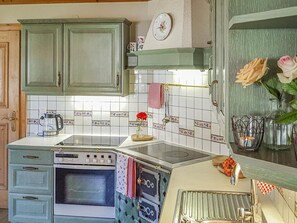 A kitchen with a built-in stove, oven, and sink, featuring vintage-style cabinets and a tiled backsplash.