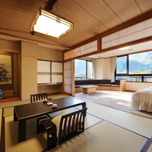 A traditional Japanese-style room with tatami flooring, a low table with cushions, a sofa, and a large window offering a view of the outdoors. - Tanigawa Hotel Nanaeyae (Nikko)