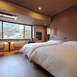 A hotel room with two beds, a wooden floor, a large window with a view of mountains, and a desk with a chair. - Tanigawa Hotel Nanaeyae (Nikko)