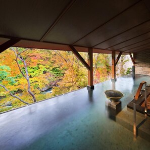 Una habitación con vistas al follaje otoñal a través de un ventanal grande, una mesa de piedra y una silla de madera.