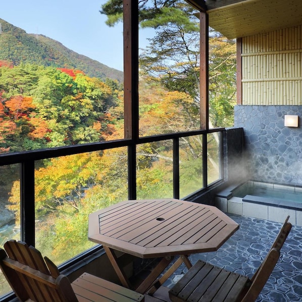 A wooden table and chairs on a balcony with a stone floor, overlooking a forested hillside. - Tanigawa Hotel Nanaeyae (Nikko)