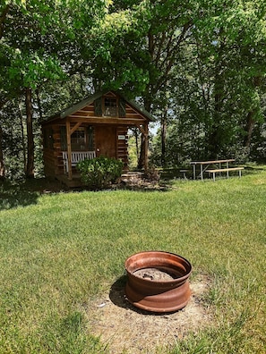 A rustic wooden cabin with a porch, surrounded by a grassy area and trees.