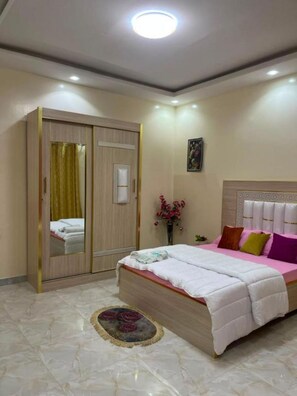 A bedroom with a bed, a wardrobe, a mirror, a vase with flowers, and a ceiling light. - Tranquil 1-bedroom apartment with AC in vibrant Dakar (Dakar)