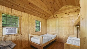 Quarto de cabana de madeira com uma cama de solteiro, uma mesa pequena e uma janela com persianas.