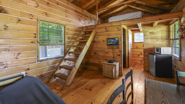 Een chaletinterieur met een houten trap, een aan de muur bevestigde televisie en een kleine kitchenette.