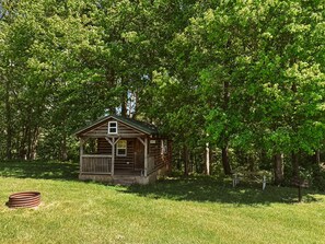 A rustic cabin with a wooden deck, surrounded by dense green trees.