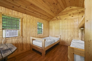 A wooden cabin room with a single bed, a small table, and a window with blinds.